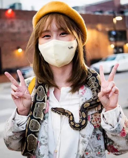 Woman wearing a mask and a snake, making peace signs