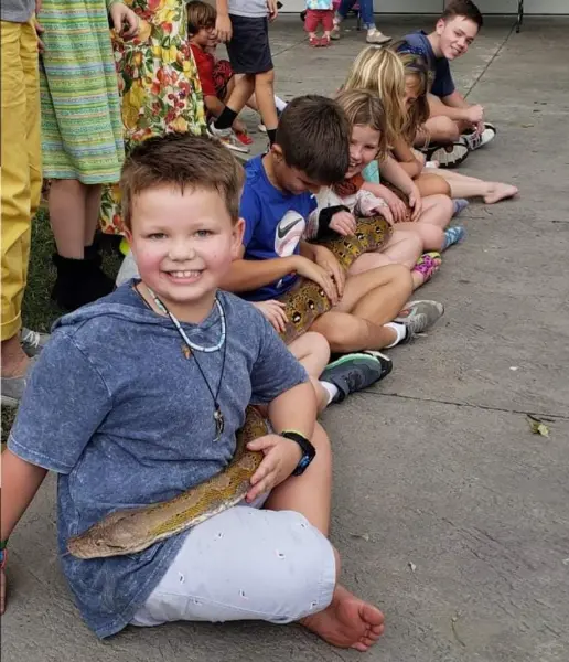 Children sitting in a line petting a large python